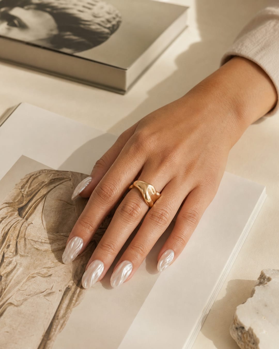 Close-up of a hand with pearl press-on nails and sculptural ring touching an art book page